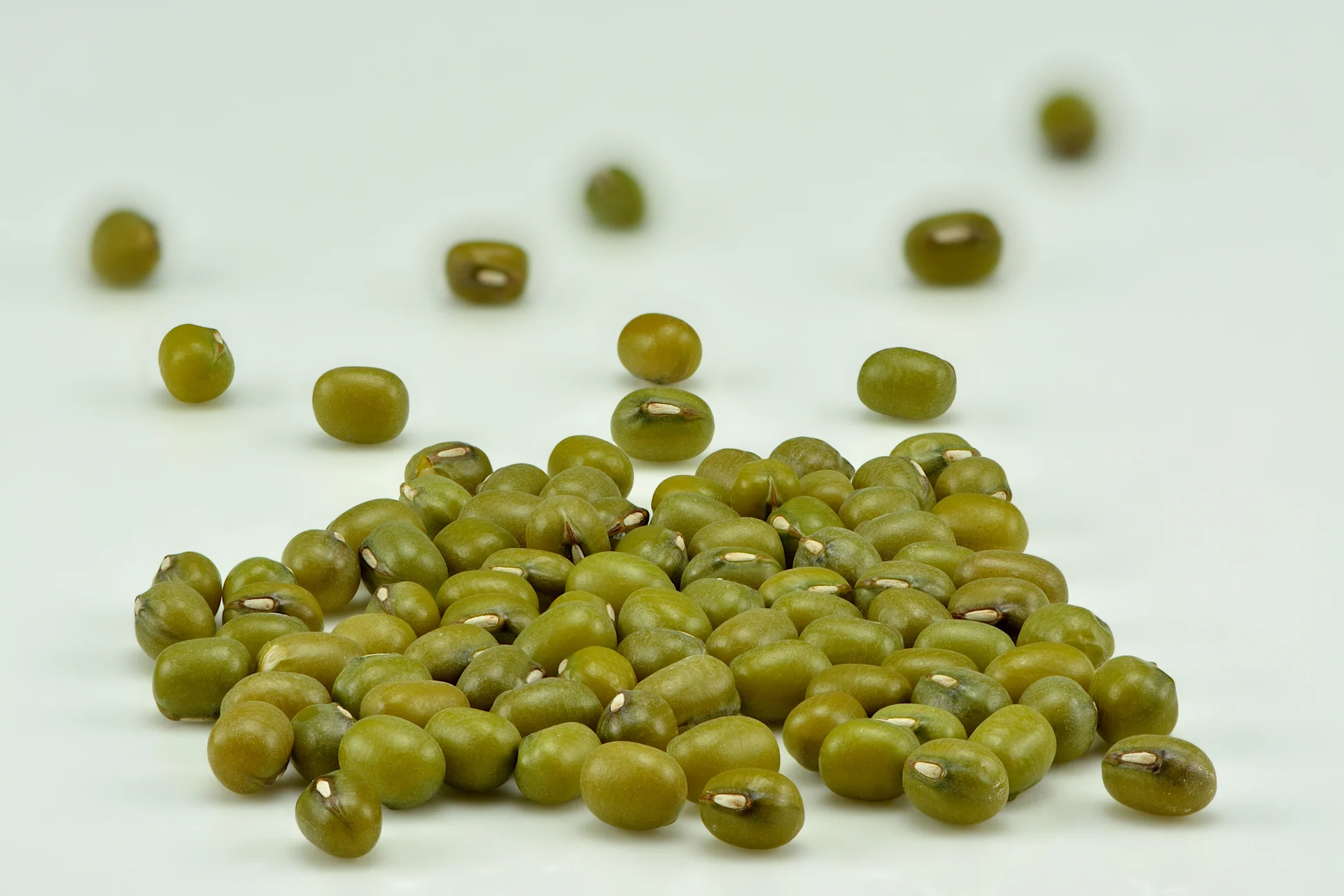 A handful of dried green gram (mung bean) seeds — small, round, olive-green beans.