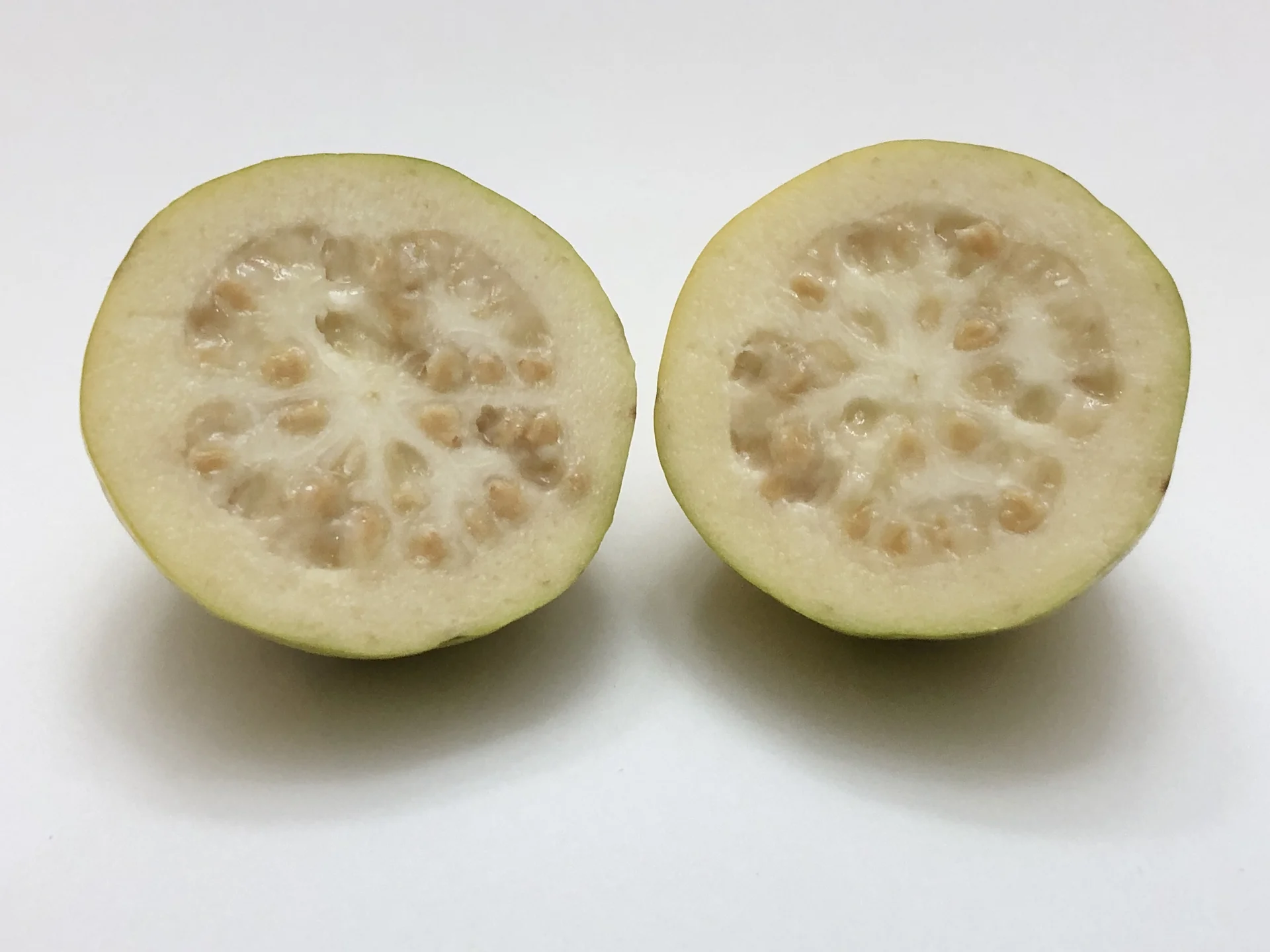 A guava cut in half showing the pale flesh and seedy centre