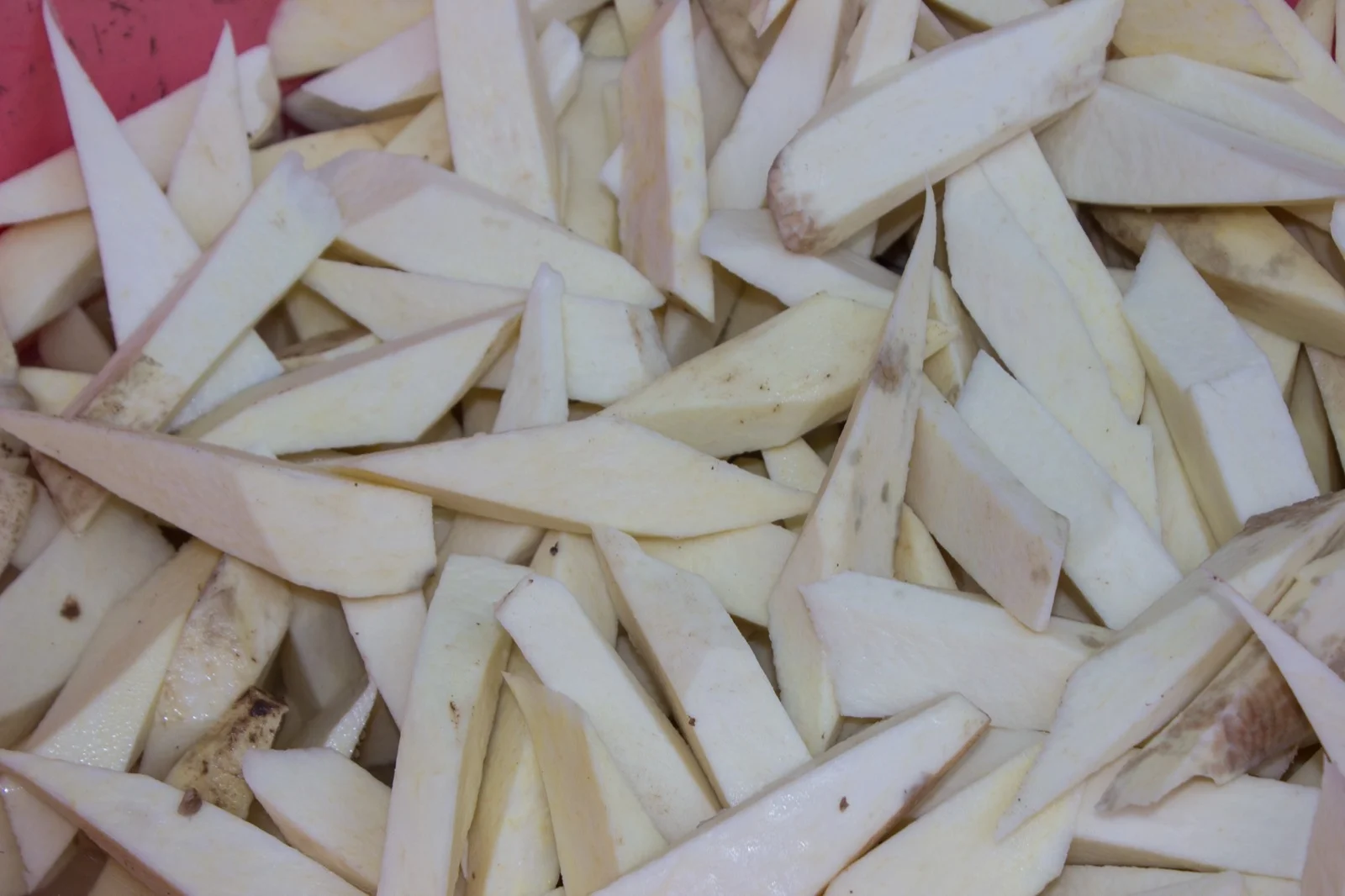 A white yam tuber cut into pieces, showing the clean, firm white flesh just under the brown skin; this is the cut-test surface a farmer checks, where nematode dry rot would show as a light-brown, crumbly layer.